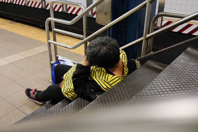 A homeless person sits on stairs to the subway platform